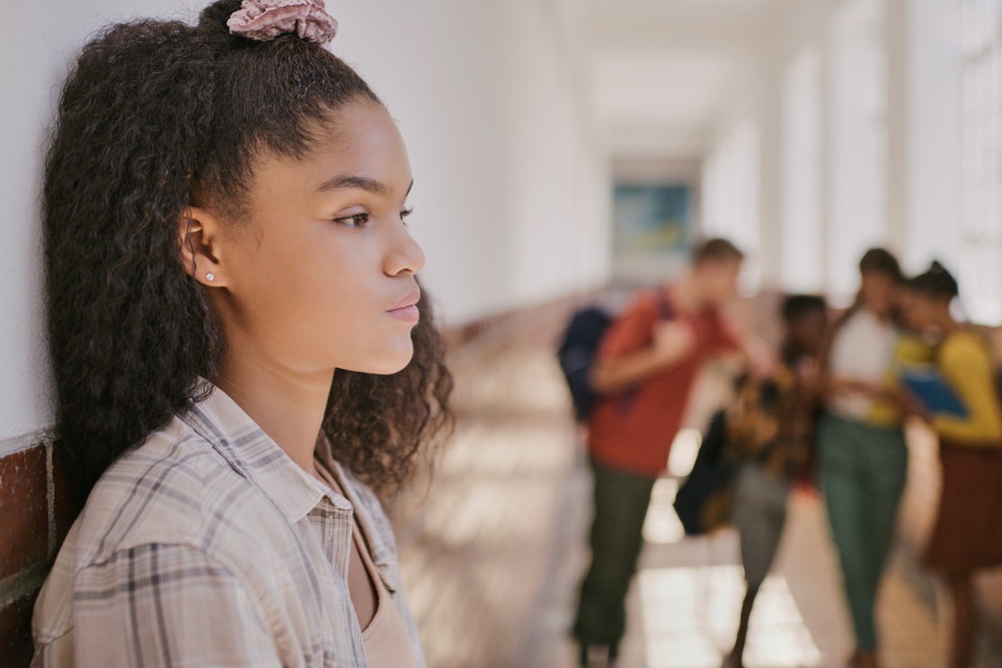 Young student leaning against a school hallway looking troubled with other students in the background