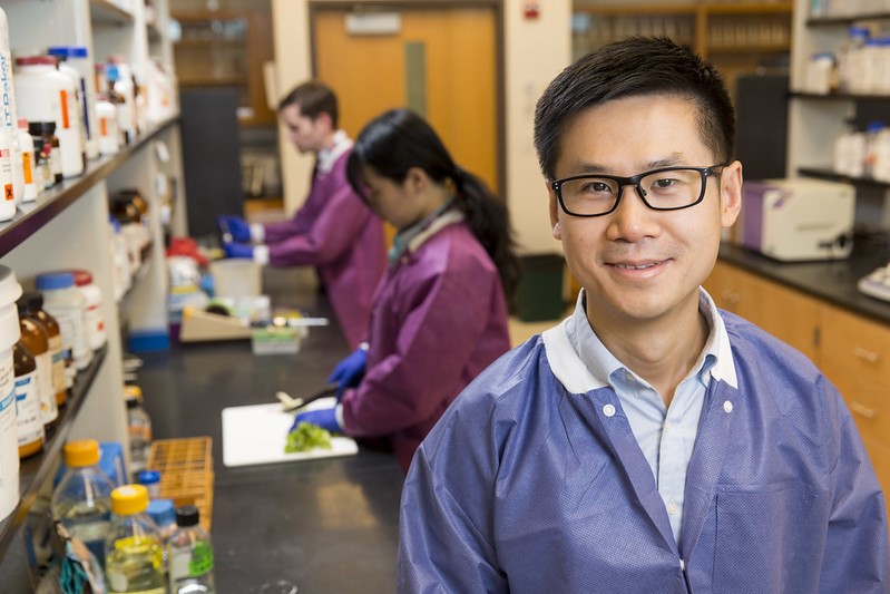 Xiangyu Deng smiles in front of two researchers working in the lab