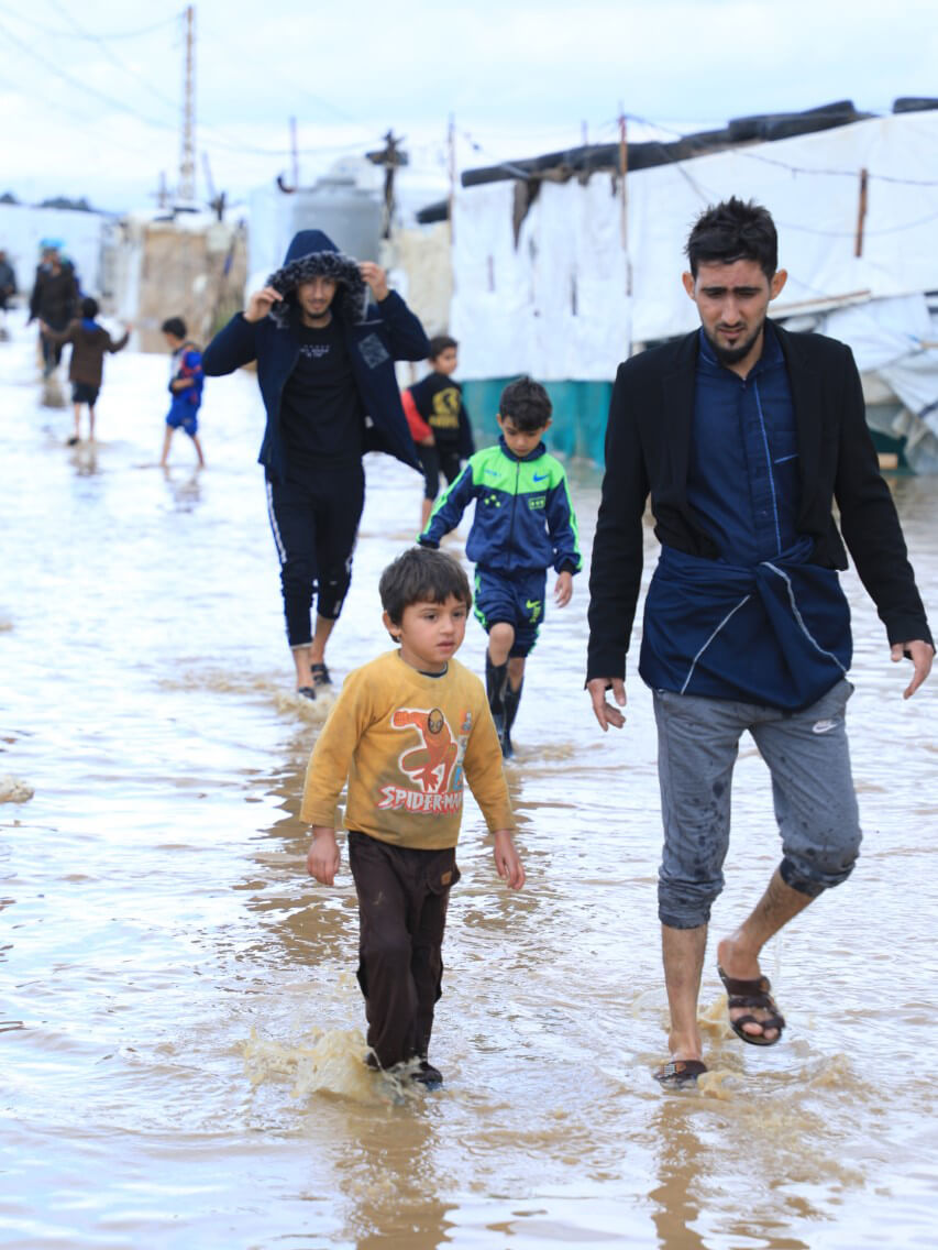 Refugees wade through possibly contaminated water among tents in the camp