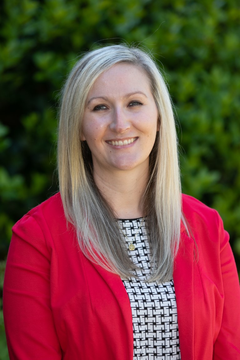 Headshot of Rochelle Sapp, who wears a red blazer in front of greenery outdoors in her professional headshot
