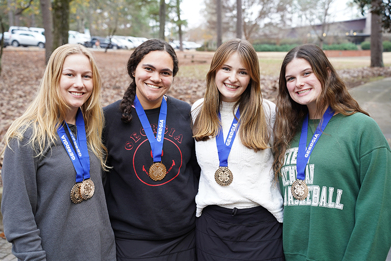Oconee County 4-H senior Consumer Judging Team members Lexi Pritchard, Alyssa Haag, Robie Lucas and Lilly Ann Smith stand side by side, smiling and wearing their team and individual medals around their necks.