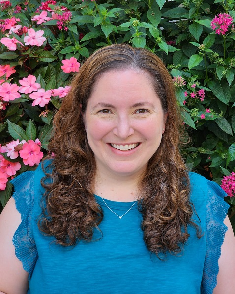 Rachel Itle smiles in front of pink flowers