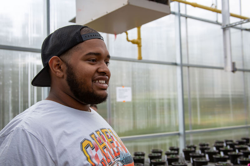 Horticulture major Braylen Thompson speaks among rows of plants in a greenhouse