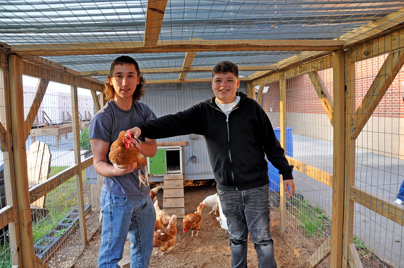 Two high-school students stand inside the chicken coop, one of them holding a brown chicken, at Archer High School in Gwinnett County.