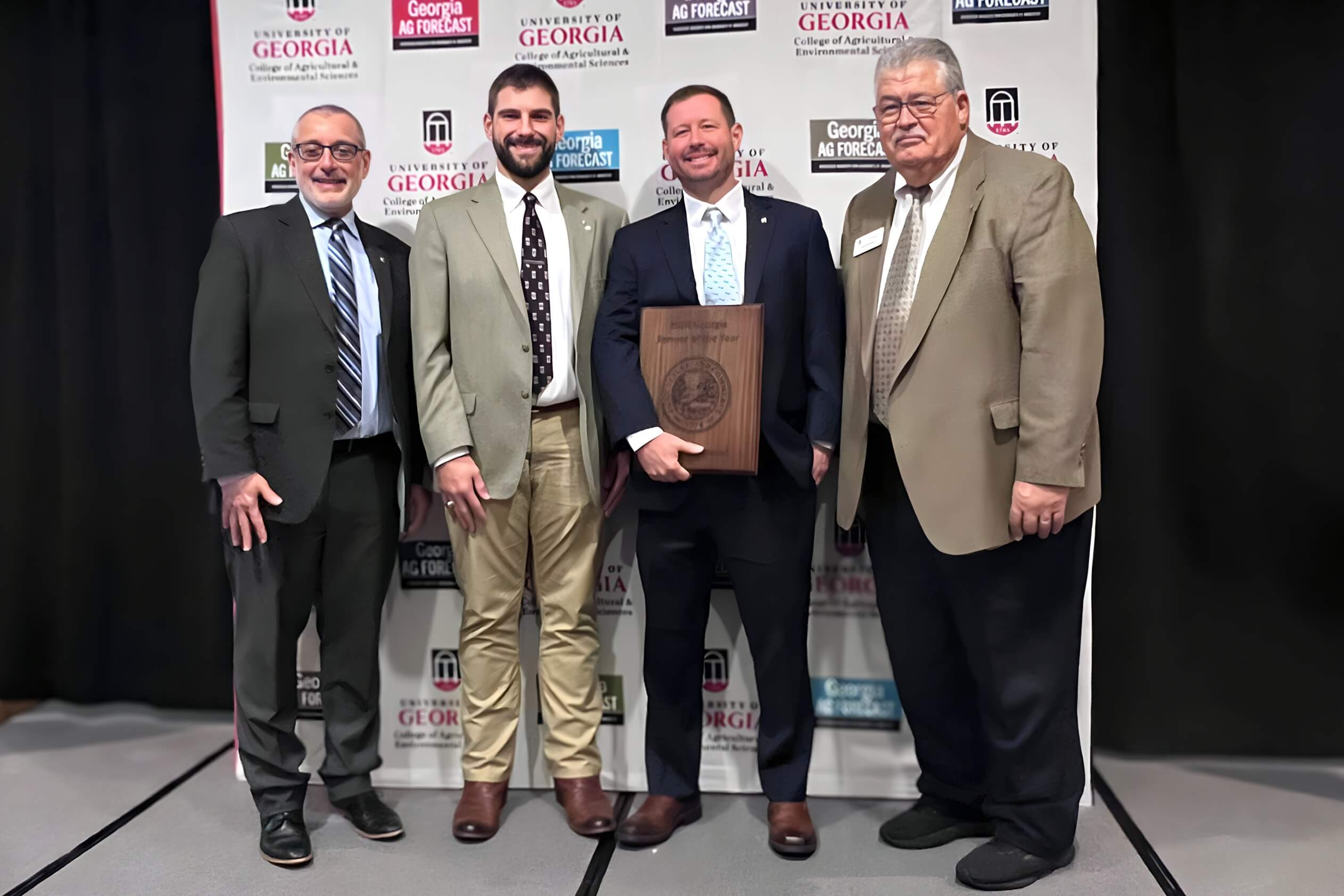 Bruce Redmond stands with CAES Dean Nick Place, his Extension Agent Blake Carter, and Associate Dean for Extension Mark McCann in front of the Ag Forecast backdrop