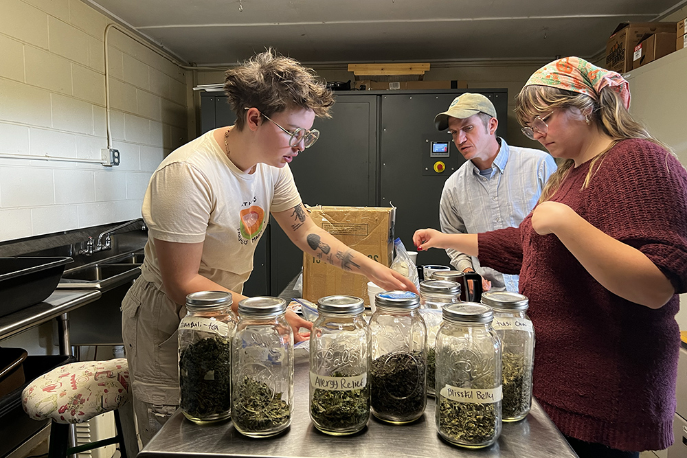 Three people stand around a table with jars of loose-leaf tea and sacks of bagged teas.