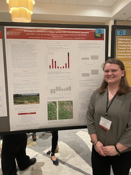 Sydney Webb stands in front of a research poster she presented in a conference setting