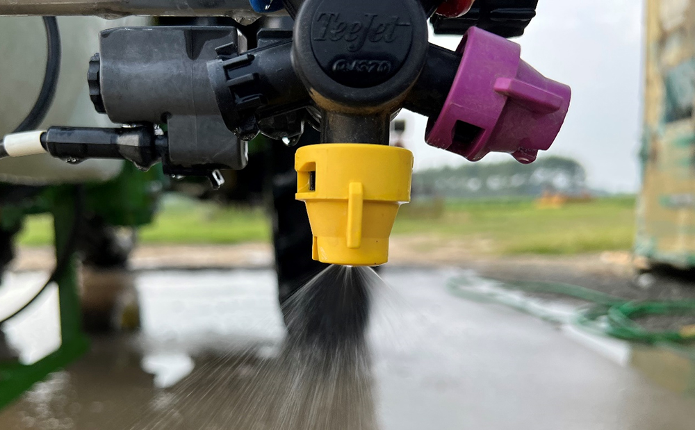 A close-up of a yellow spray nozzle pointed downwards and spraying water
