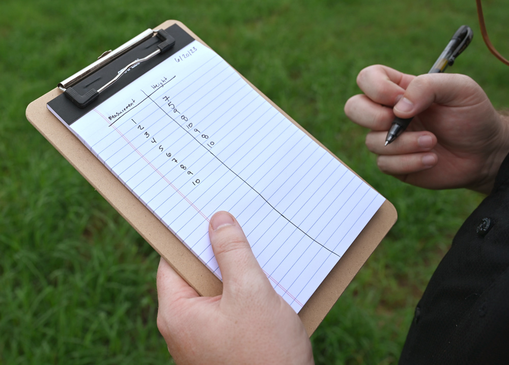 A table is drawn on a paper notepad to record the height of each location and how many locations were measured in a field.