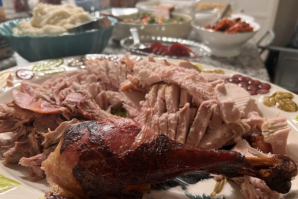 A platter of sliced turkey and a roasted turkey leg, surrounded by bowls of mashed potatoes, salad and other holiday sides.