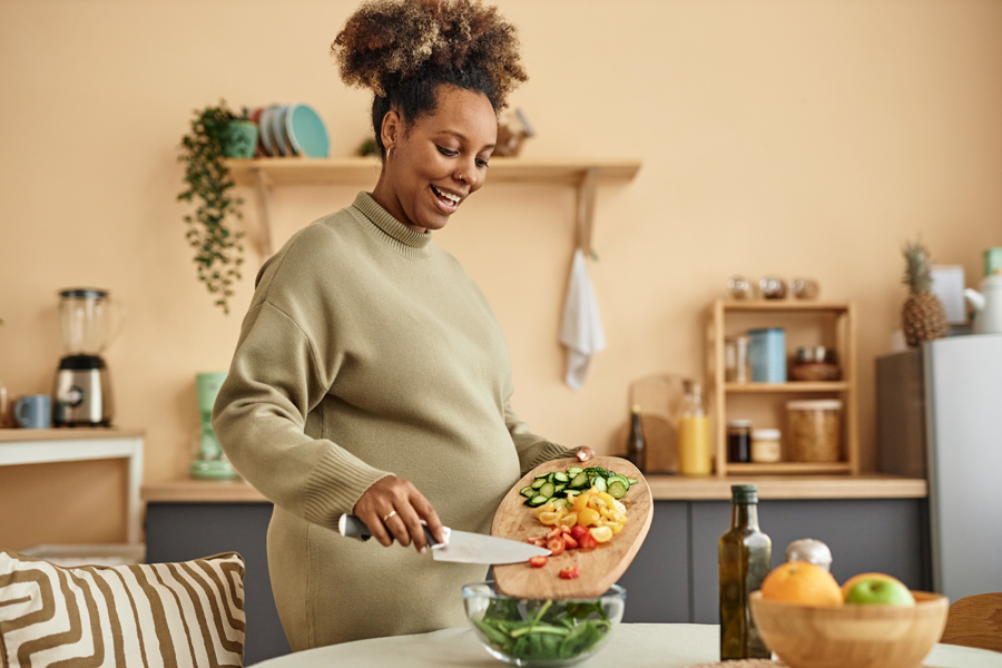 A woman holds a cutting board and a knife and is moving vegetables from the cutting board into a bowl.